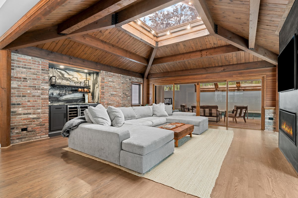 Vaulted living room with exposed wood beams, skylight, brick accent wall, and linear fireplace
